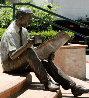 statue of man sitting in a steps reading a paper