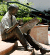 statue of a man sitting in a bench reading a paper