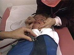 Health care worker holds stethoscope to child's chest. Another person holds the NG tube in place at child's nose.