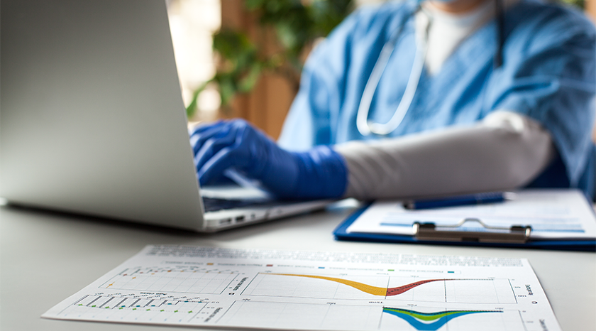 Epidemiologist looking at laptop with a binder and chart. 